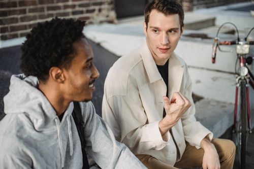 Free High angle of positive young multiethnic male friends in stylish clothes chilling on city street and chatting on sunny day Stock Photo