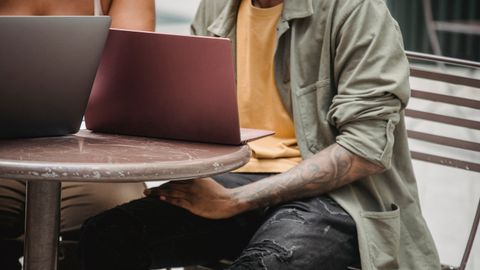 Crop anonymous multiracial man and woman sitting at round table with laptops while working remotely together on startup in cafe