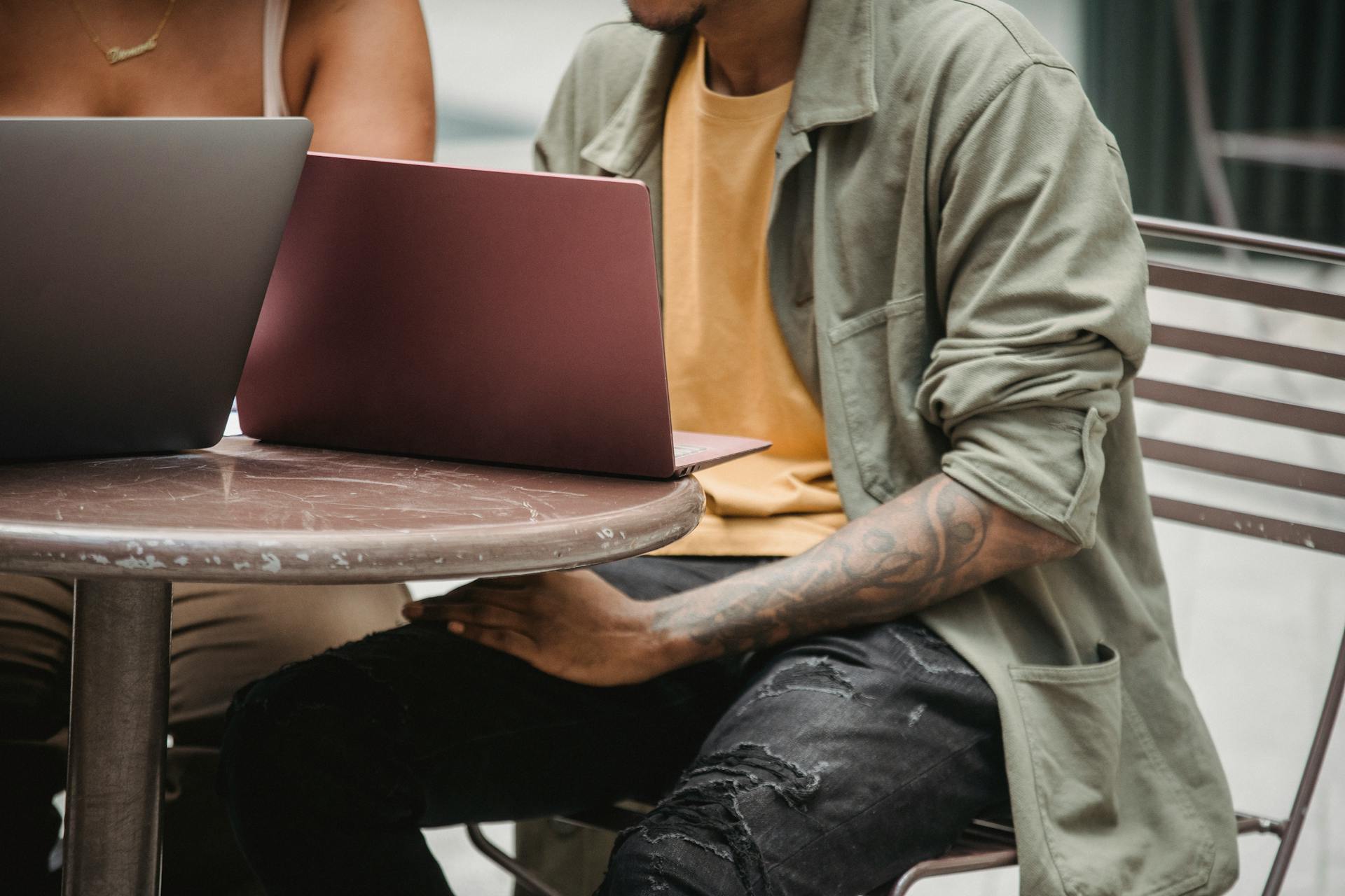 Crop anonymous multiracial man and woman sitting at round table with laptops while working remotely together on startup in cafe