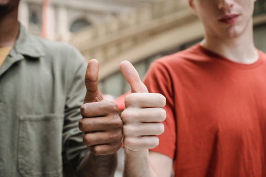 Crop anonymous diverse male friends in casual outfits demonstrating thumbs up gesture while standing together on city street - Fotografer Sidoarjo