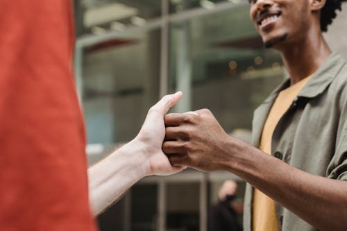 Crop positive multiethnic guys shaking hands on street