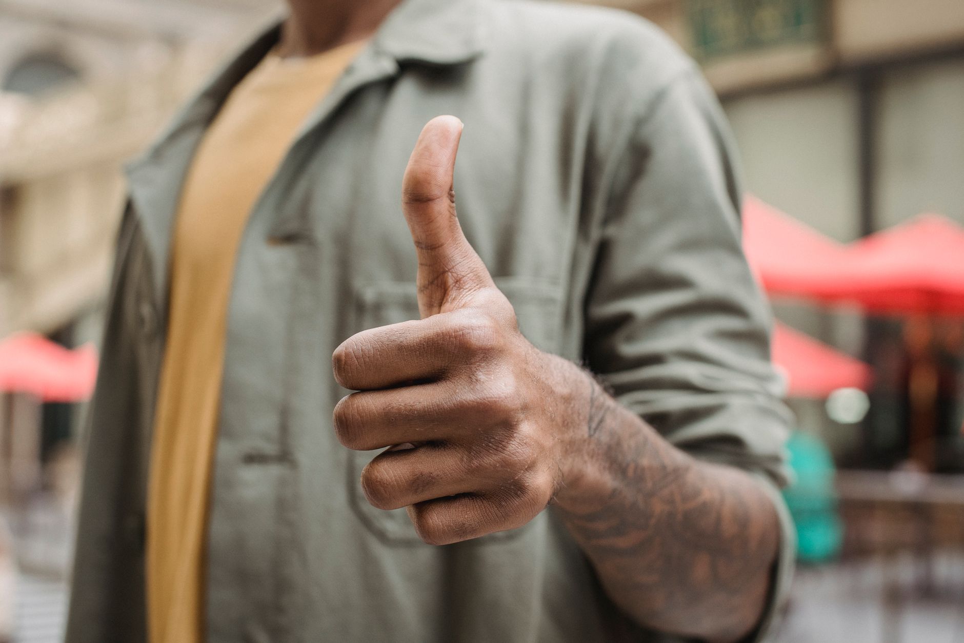 Crop faceless young black male in casual outfit standing on city street and showing thumb up gesture