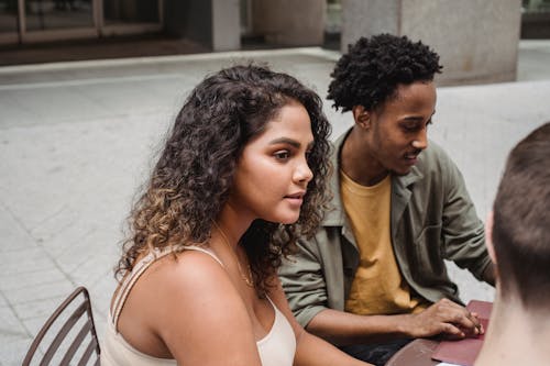 High angle of concentrated young Hispanic lady with curly hair sitting and table with diverse male colleagues and discussing business plans in street cafe