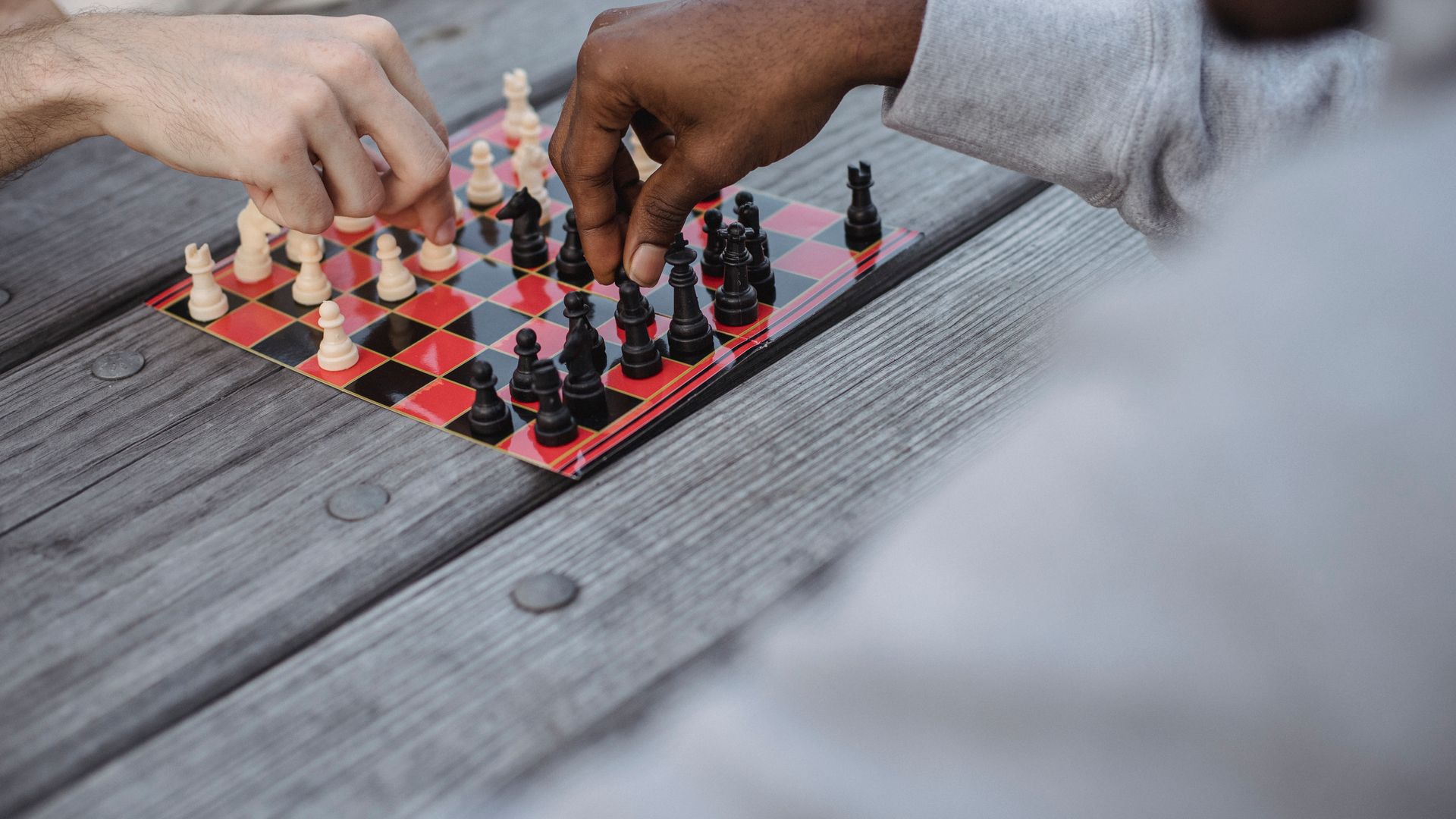High angle of crop faceless young diverse male friends playing chess sitting at wooden table in daylight — popular strategies