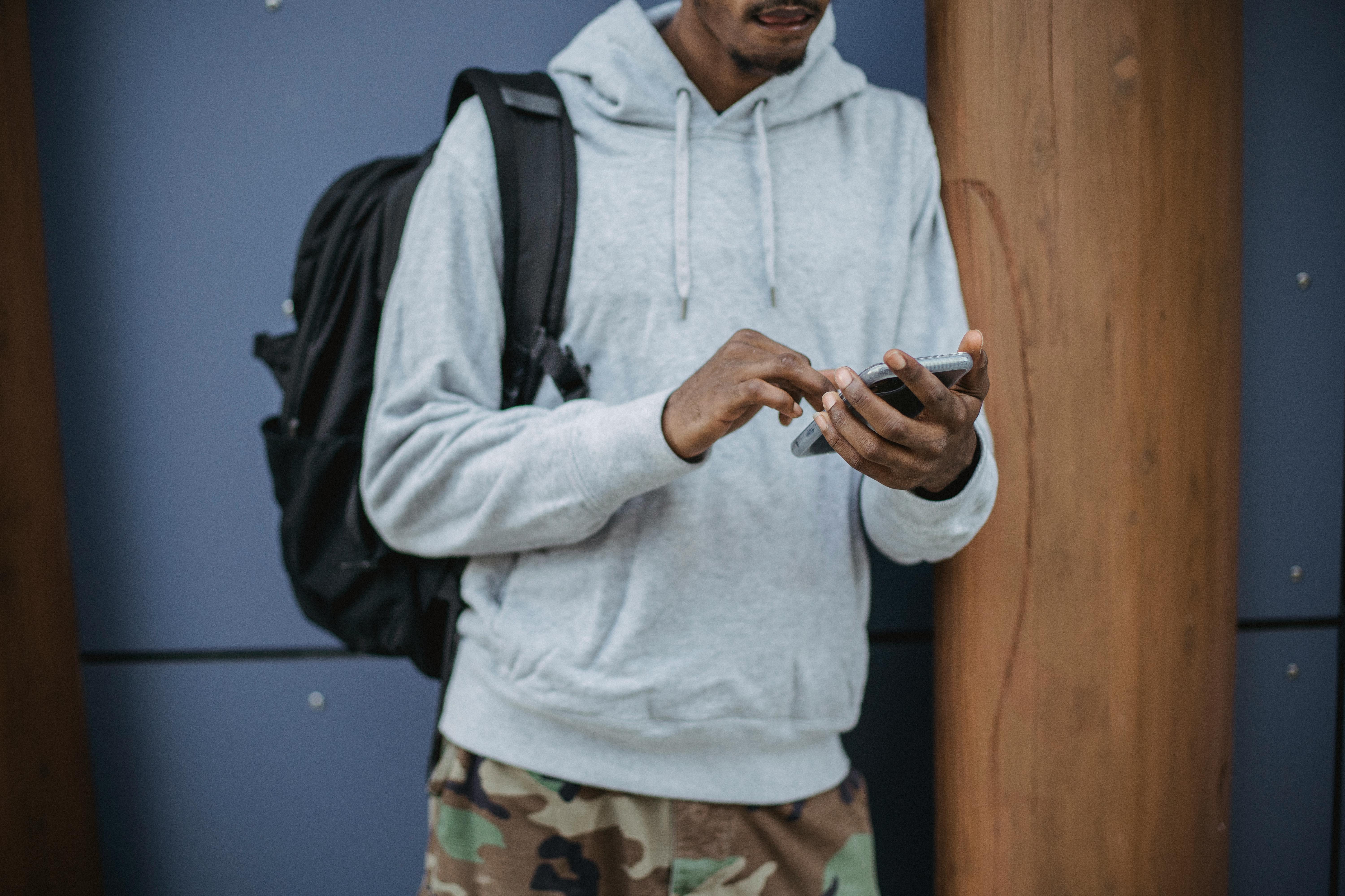 unrecognizable ethnic man messaging on smartphone near modern building