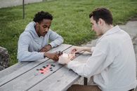 Concentrated young multiethnic male friends in casual clothes sitting at table in park and playing chess game