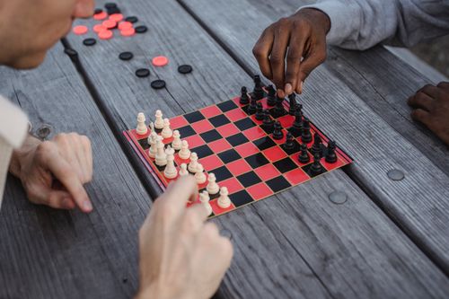 Free From above of crop anonymous focused multiethnic male friends playing chess board game sitting at lumber table in park Stock Photo