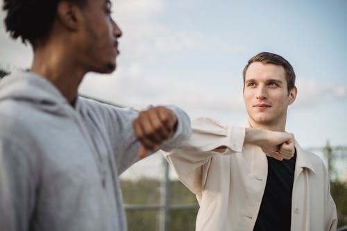 Free Serious multiethnic male friends doing elbow bump for protection and avoiding spreading of coronavirus infection and looking at each other Stock Photo