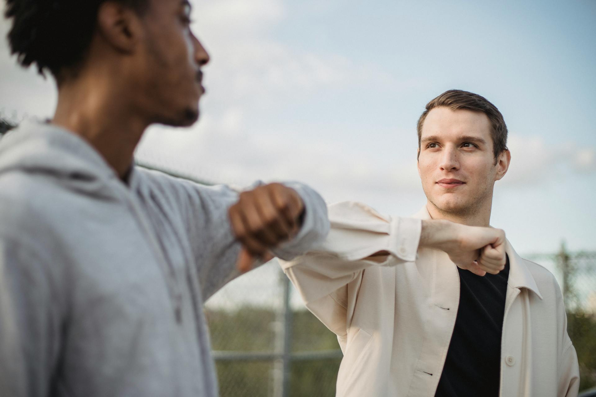 Serious multiethnic male friends doing elbow bump for protection and avoiding spreading of coronavirus infection and looking at each other