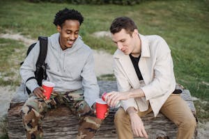 High angle of male pouring carbonated drink from tin can to smiling black friend sitting with red cup