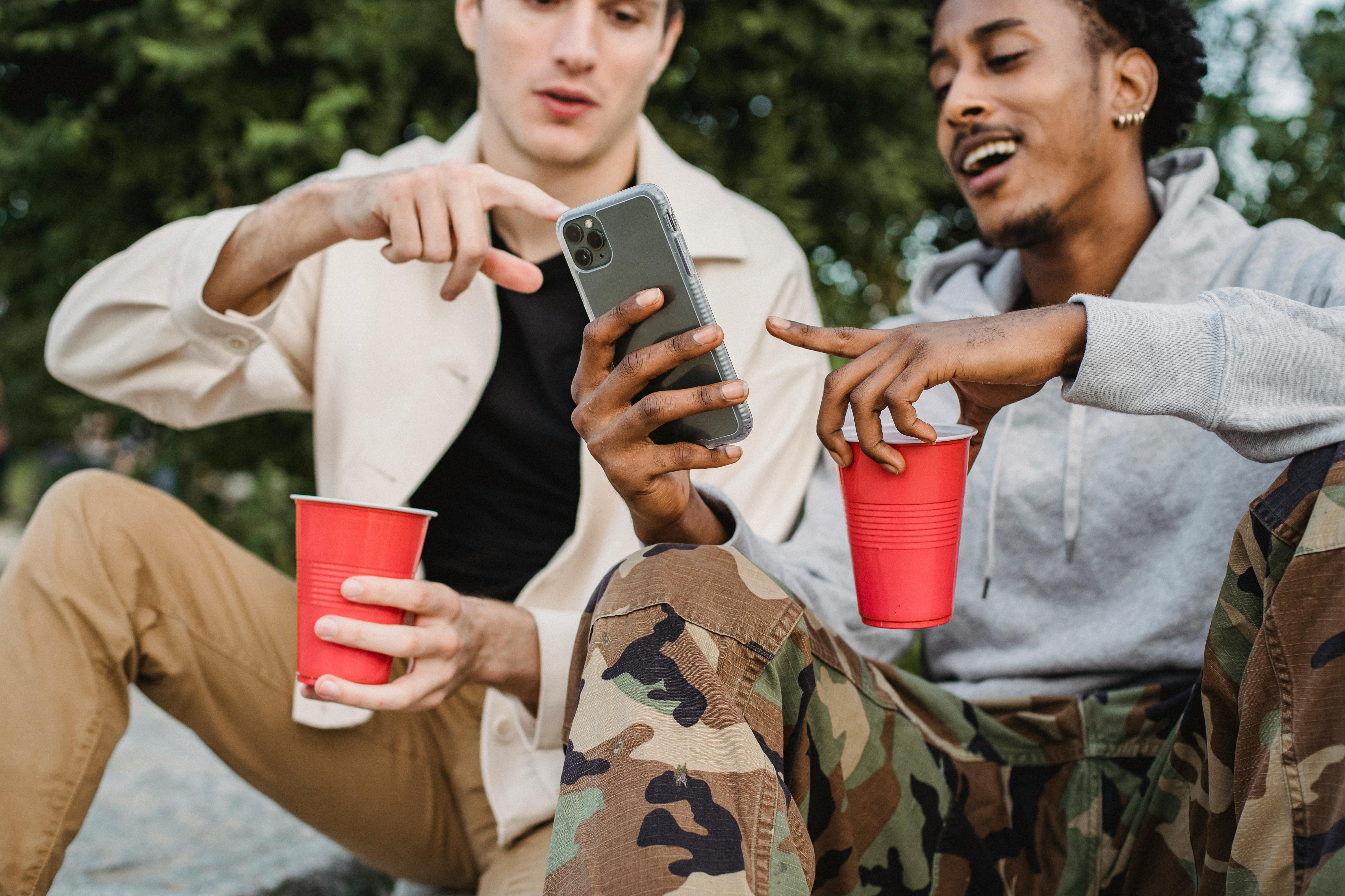 multiethnic friends using smartphone together sitting with cups