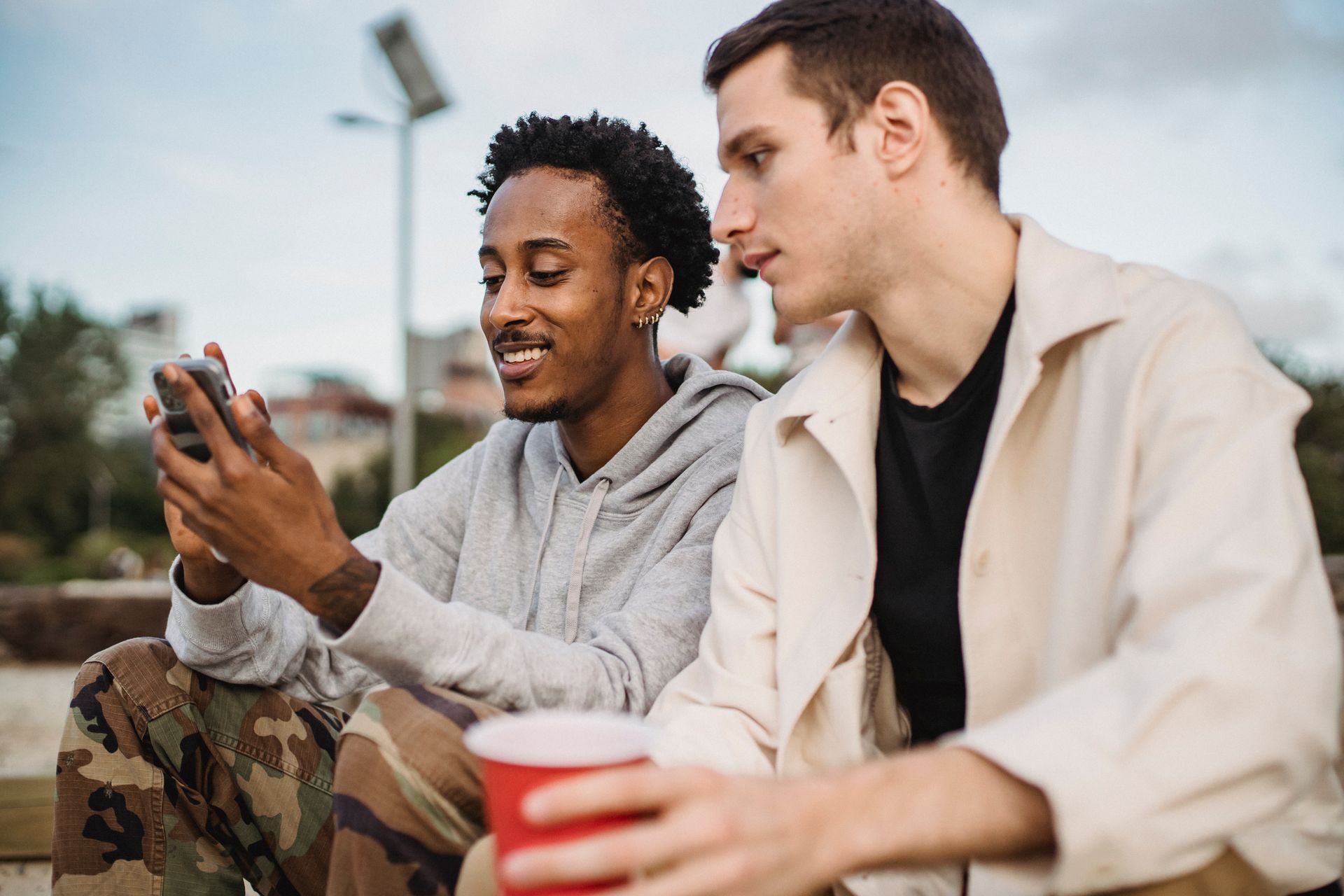 Two young men bonding over social media outdoors, sharing a moment with a smartphone.