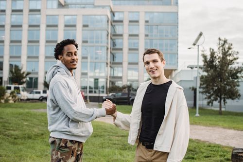 Free Young diverse male friends shaking hands while standing on lawn against modern building and looking at camera Stock Photo