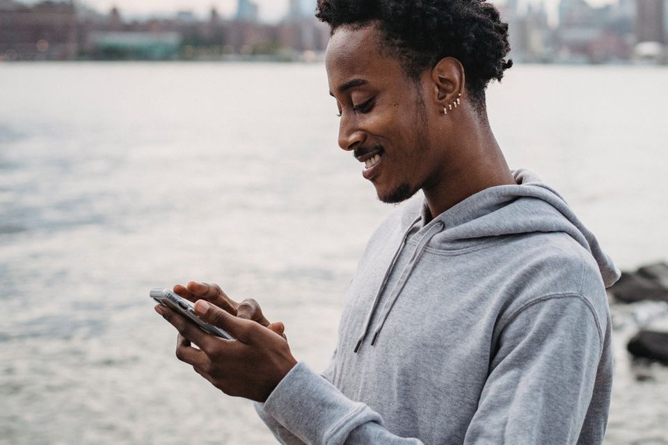 A smiling man scrolling on his phone by a river