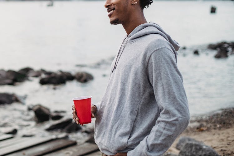 Positive Black Man With Red Cup Standing On Riverside