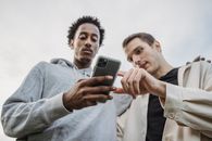 Multiethnic friends browsing smartphone together outside