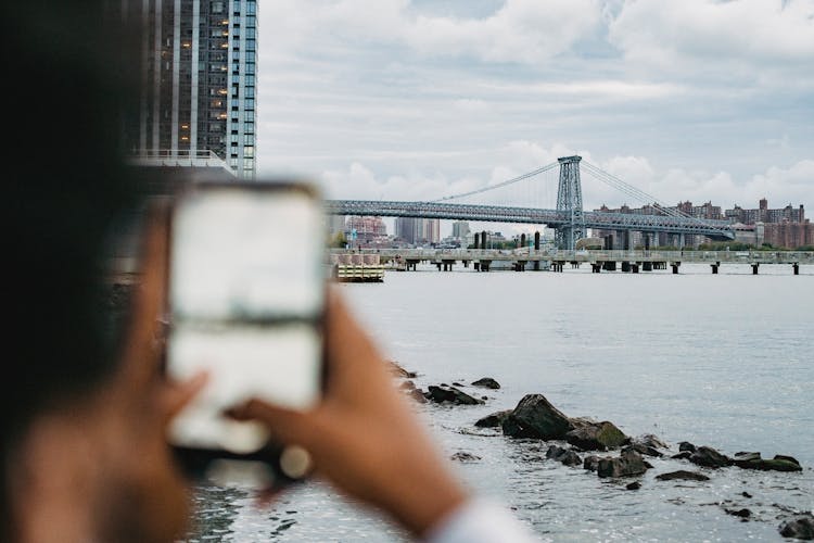 Black Man Taking Picture Of Bridge On River Bank