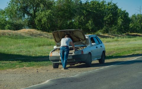 A driver standing beside his car on the roadside inspecting an issue
