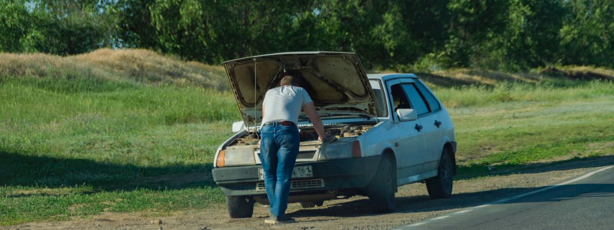 Hombre revisando un coche averiado en el arcén
