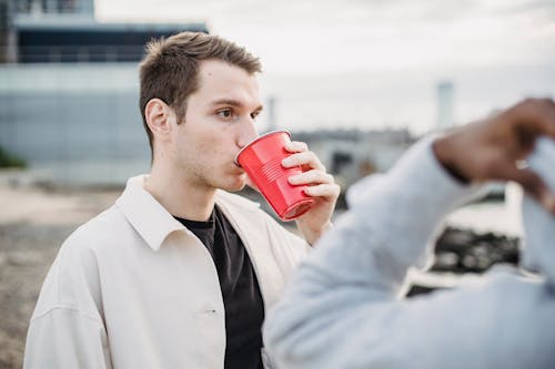 Young man drinking beverage from plastic cup with black friend
