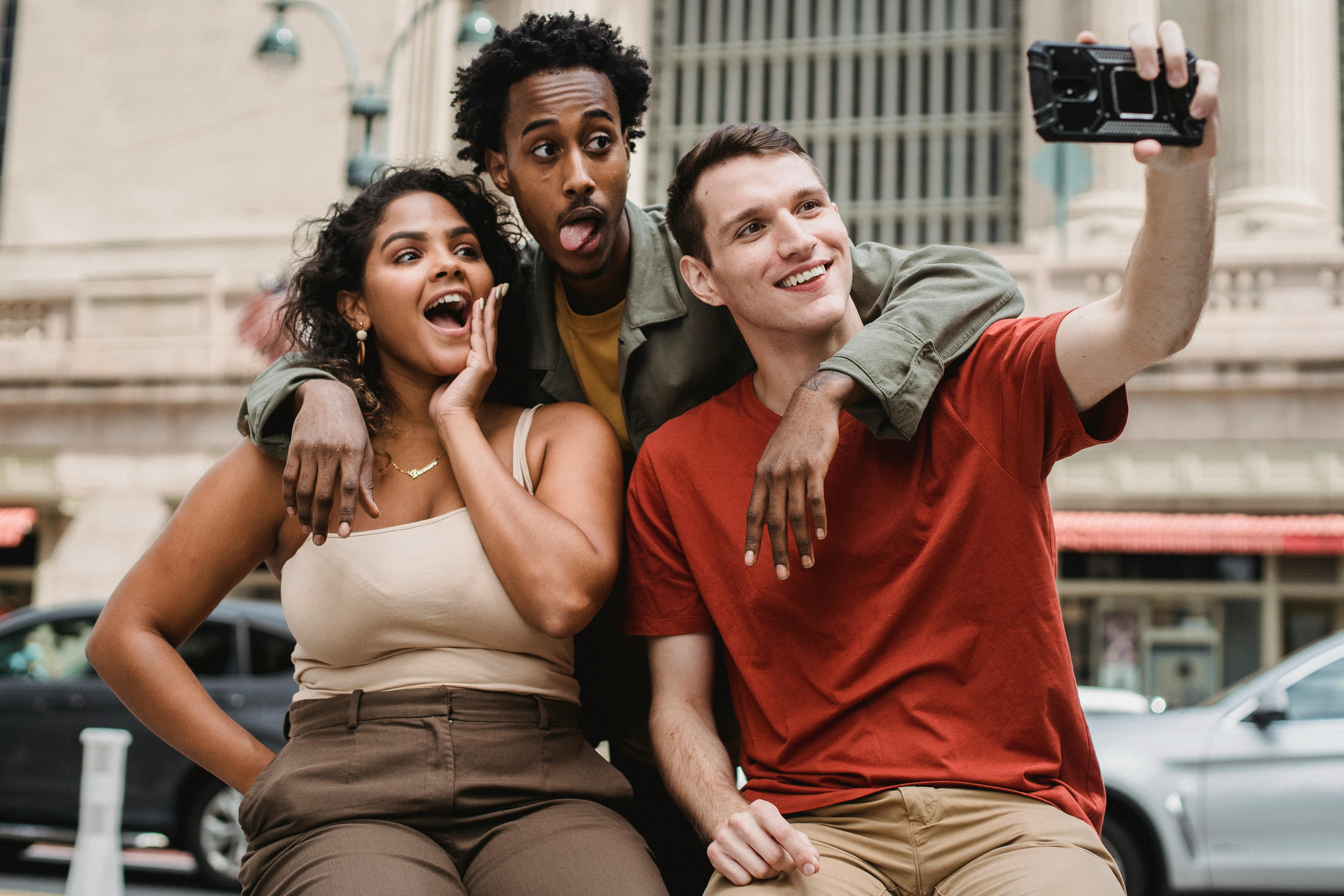 smiling multiracial friends taking selfie in street