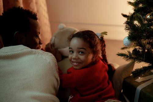 Free A joyful dad and daughter spend Christmas Eve bonding near a decorated tree indoors. Stock Photo