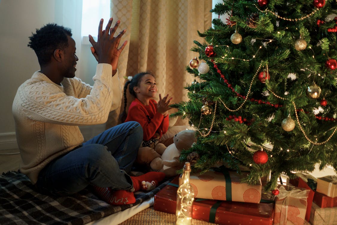 Dad and Daughter Sitting and Clapping Near a Christmas Tree