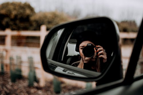 A Woman Taking Selfie Using Dslr Camera on the Side Mirror