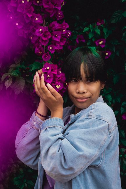 A woman smiles while holding vibrant bougainvillea flowers, showcasing natural beauty.