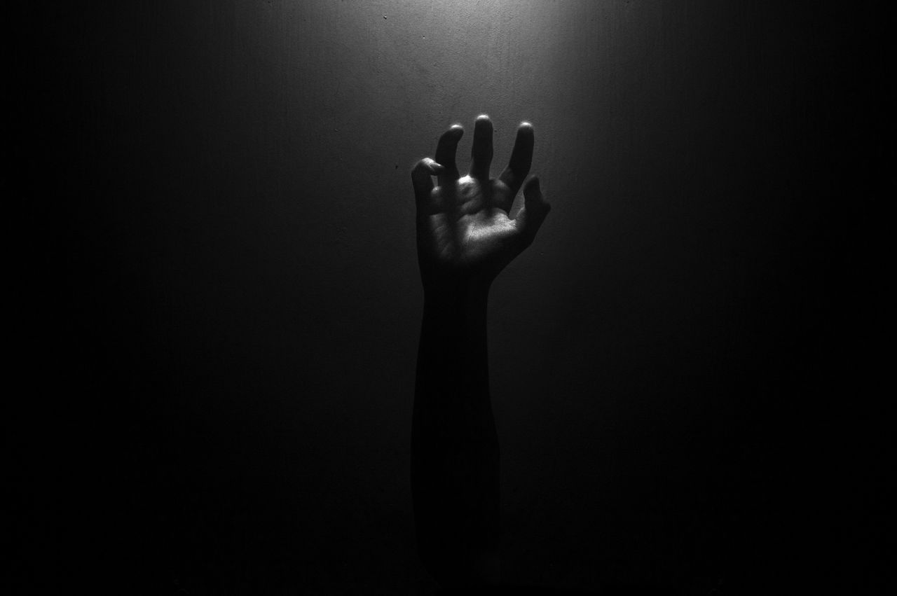 a solitary hand reaching upward contrasted against a dark backdrop cre