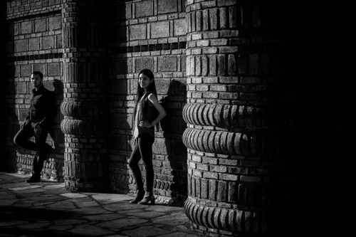 Free Artistic black and white photo of a couple posing by an ancient brick wall. Stock Photo