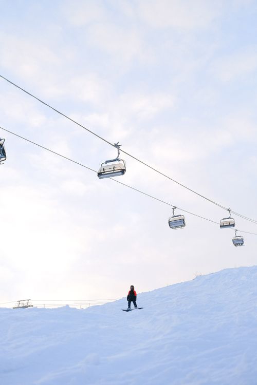 Free A solitary snowboarder beneath cable cars on a snowy mountain, highlighting winter sports. Stock Photo