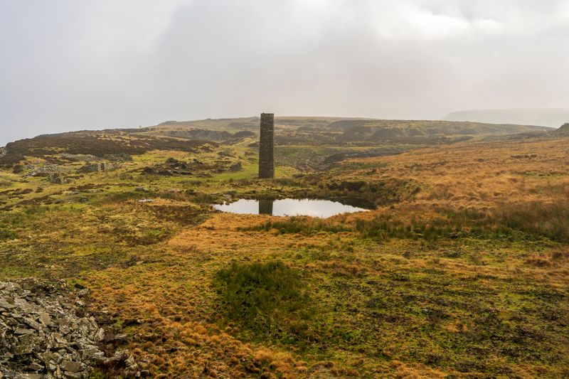 A serene moorland scene with a tower reflecting in a calm pond under misty skies.