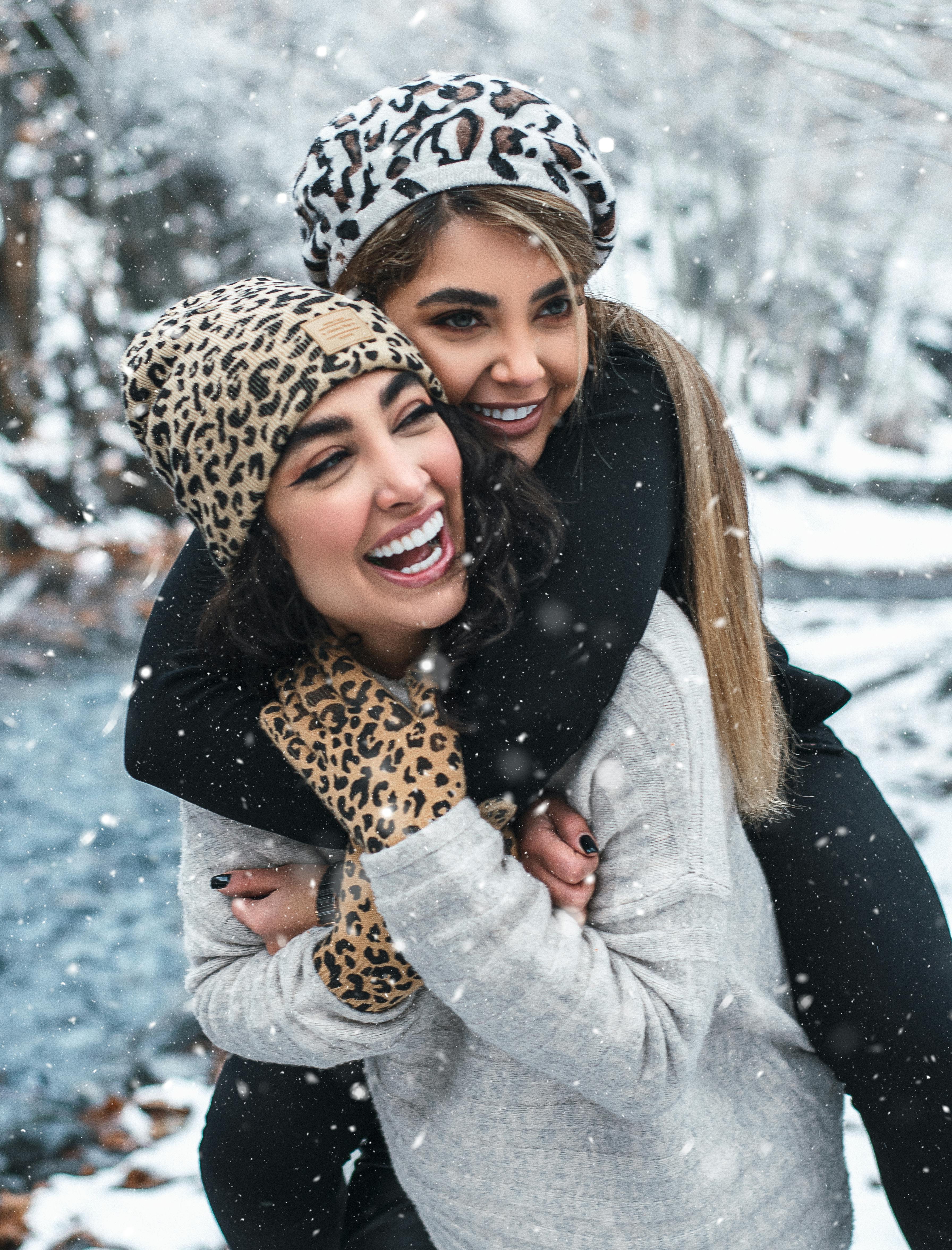 laughing woman carrying girlfriend on back in winter forest