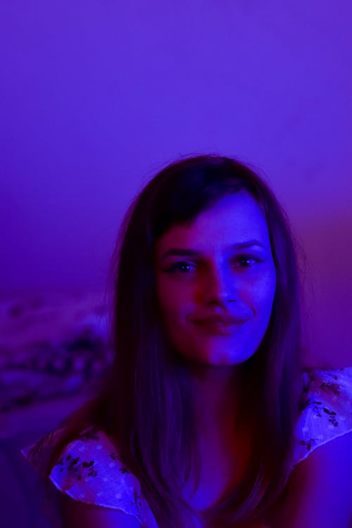 Positive female with long hair in casual wear in dark room with violet light looking at camera