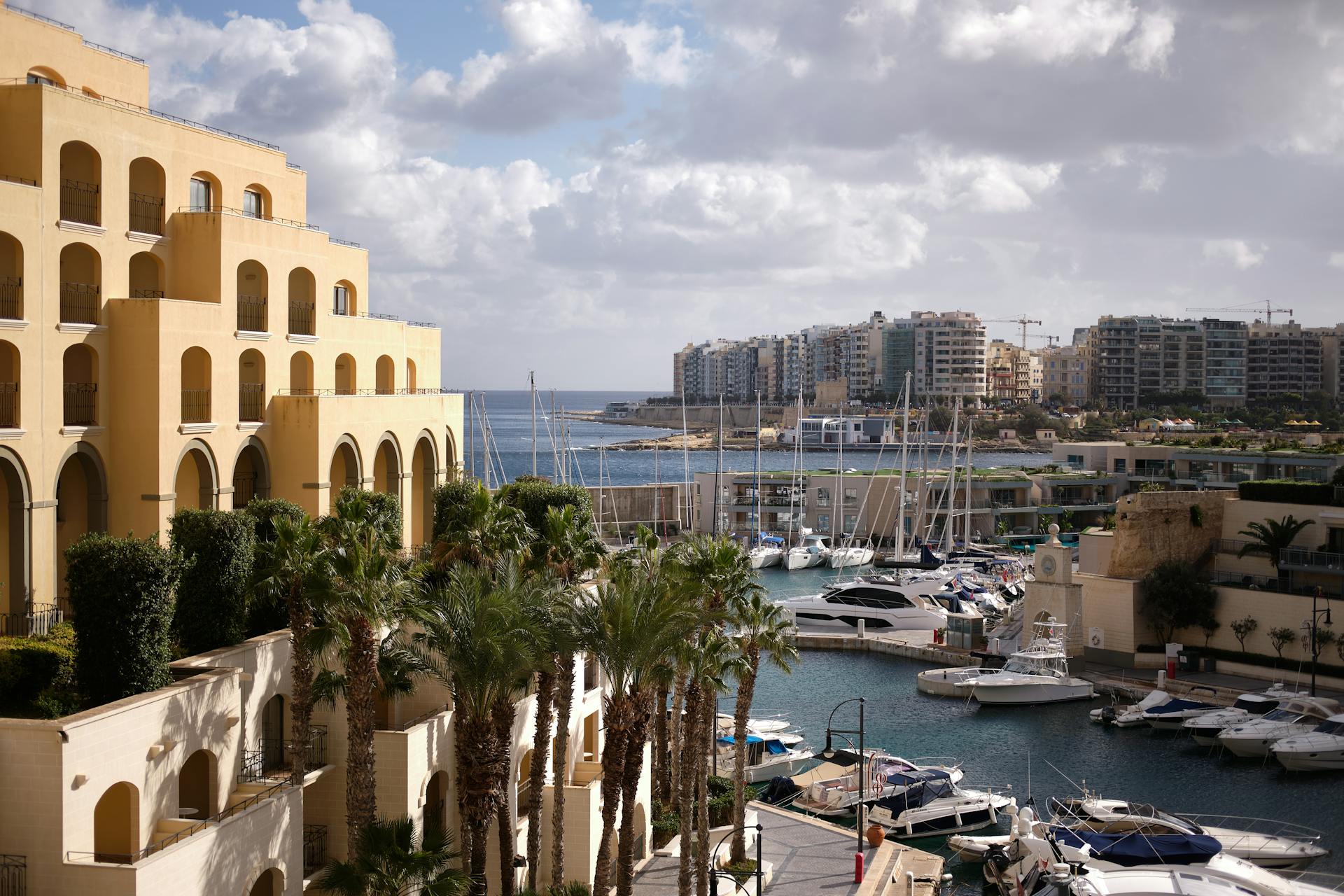 Scenic view of Hilton Malta's marina with yachts and palm trees, capturing urban luxury by the sea.