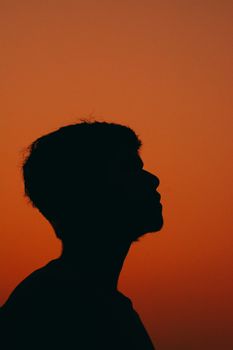 A man's silhouette stands against a vivid orange sunset sky, evoking tranquility and contemplation.