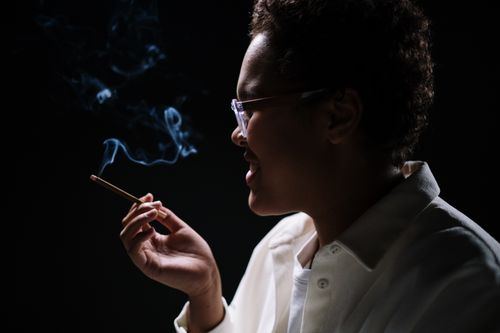 Free Side profile of a woman smoking with visible smoke against a dark background. Stock Photo