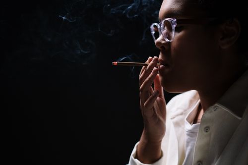 Free Side view portrait of a woman smoking a cigarette in a dark setting, wearing eyeglasses. Stock Photo
