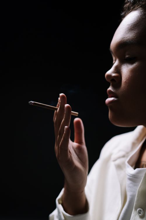 Free Side view of a woman smoking in a dark room, emphasizing shadows. Stock Photo