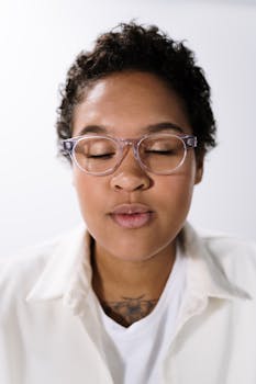 Close-up studio portrait of a young woman with curly hair and eyeglasses, eyes closed and calm.