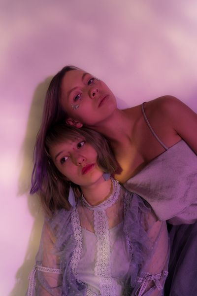 Two performers leaning together in lilac light — Darya Sannikova on Pexels