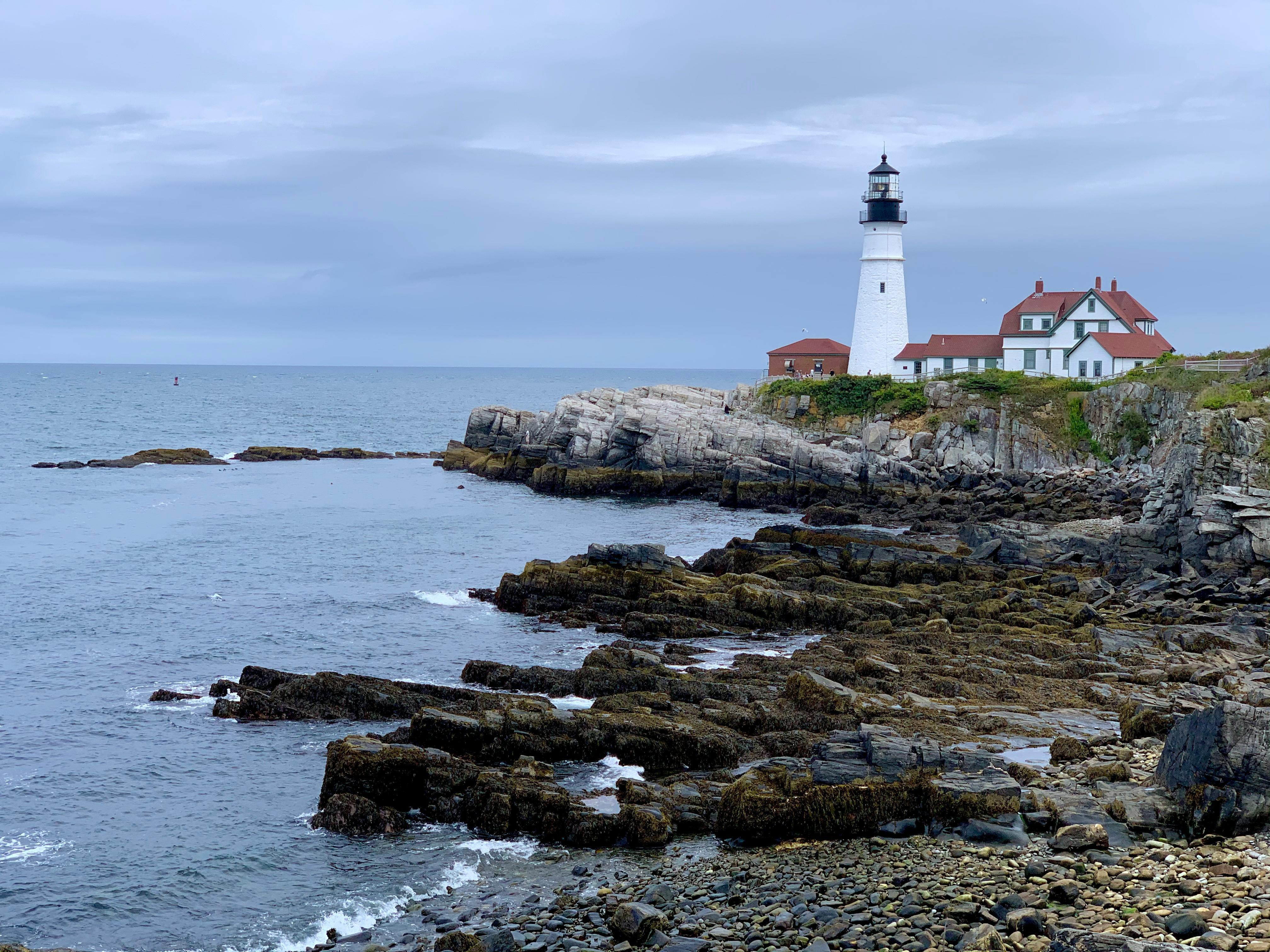 A picturesque lighthouse standing on rocky cliffs by the serene sea under a cloudy sky.