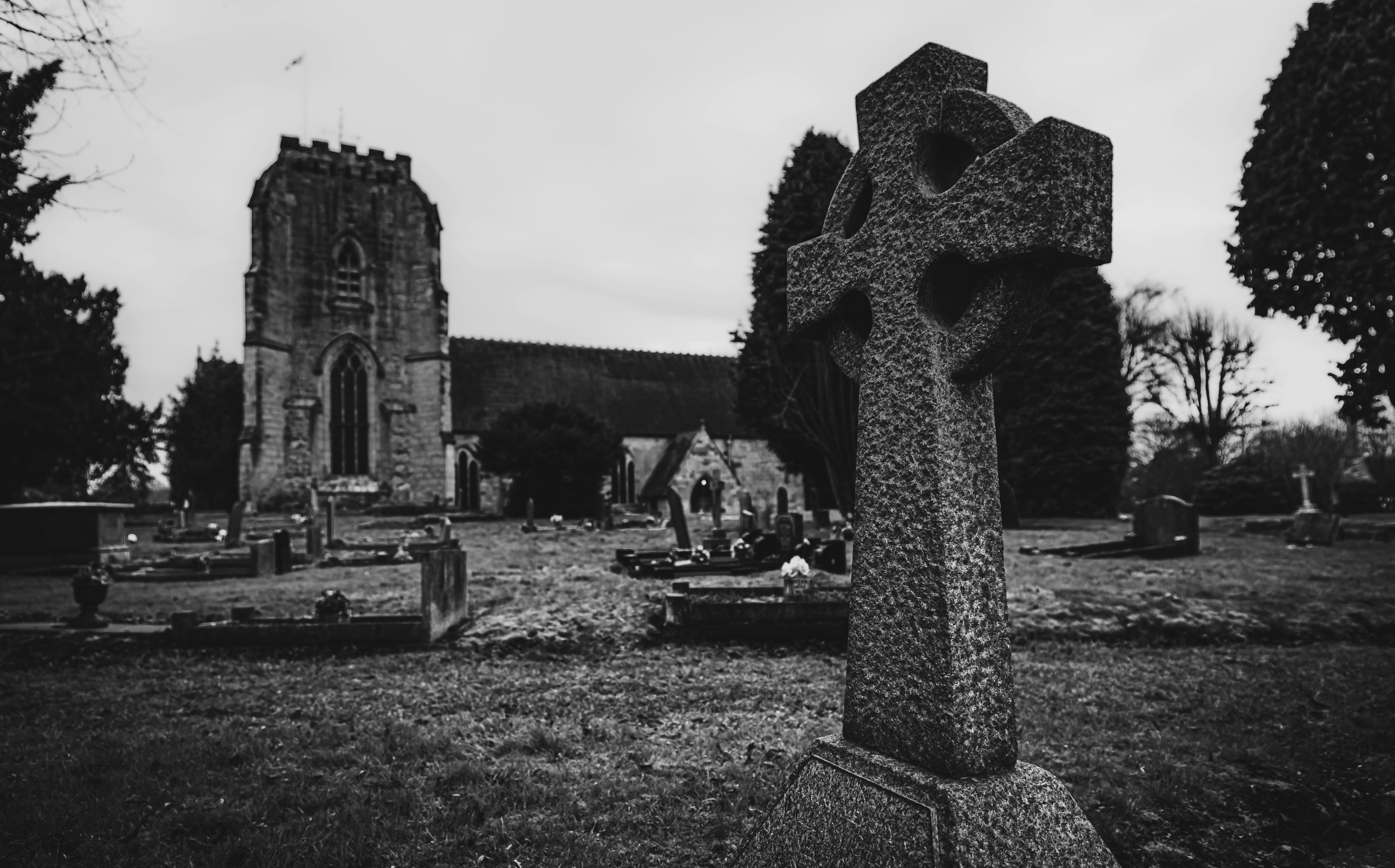 A black and white photo of a cemetery with a Celtic cross in Polesworth, England featuring historic church architecture.