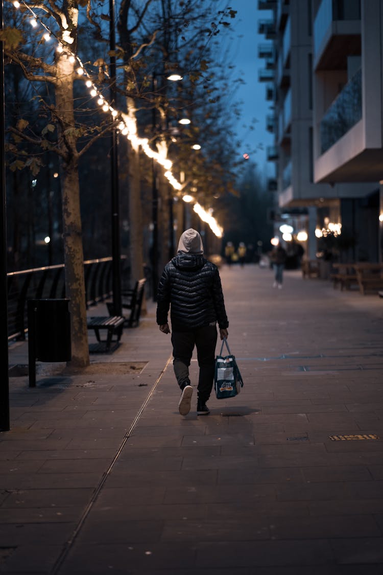 A Back View Of A Person Walking On The Street At Night