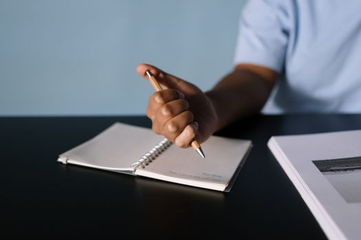 A person writing in a notebook, focusing on the hand holding a pen.