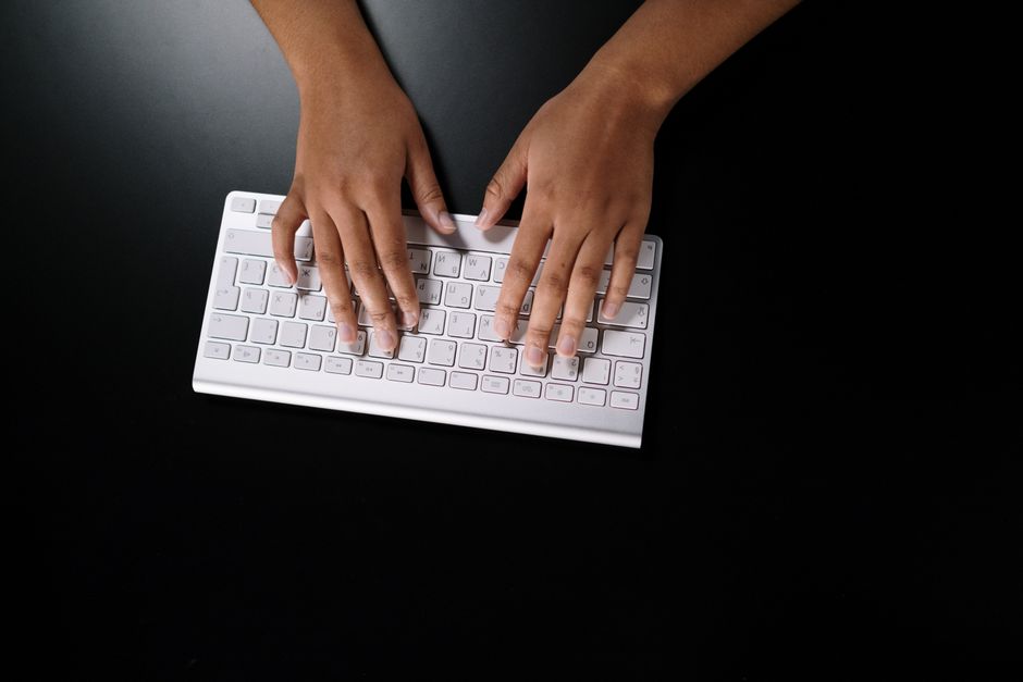 Overhead view of hands typing on a sleek white keyboard on dark surface.