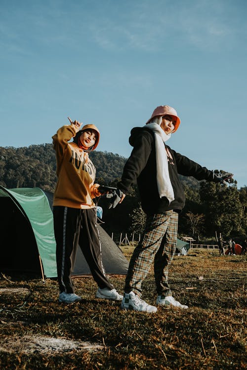 Free Full body of ethnic female friends in casual clothes standing near camp tent in meadow Stock Photo
