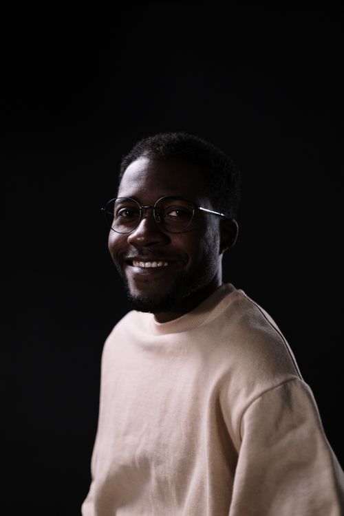 Free Portrait of a smiling man wearing glasses indoors on a dark background. Stock Photo