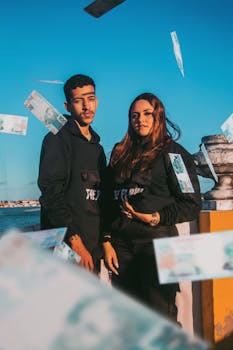 A couple poses outdoors with banknotes falling around them, enjoying sunlight and wealth.